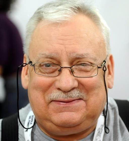 Martwa natura z otwartą książką z sagi o Wiedźminie, piórem, kałamarzem i mapą Kontynentu, symbolizująca twórczość Andrzeja Sapkowskiego.