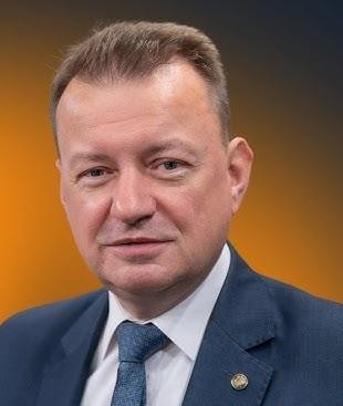 Mariusz Błaszczak jako Minister Obrony Narodowej, w otoczeniu wojskowym, symbolizujący jego rolę w obronności kraju.