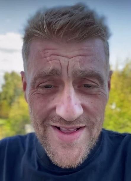 Tomasz Jakubiak w kitlu szefa kuchni, z uśmiechem prezentuje danie na talerzu w nowoczesnej kuchni.