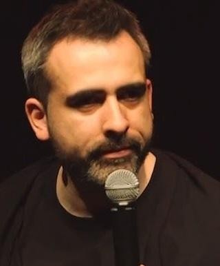 Abelard Giza podczas występu stand-upowego na scenie, z mikrofonem, w otoczeniu świateł scenicznych.