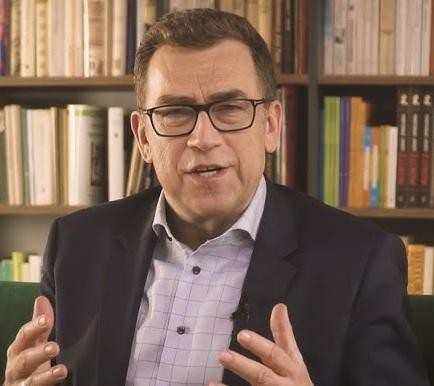 Maciej Orłoś w ujęciu z filmu, w roli aktorskiej, z intensywnym wyrazem twarzy, w klimatycznym oświetleniu.