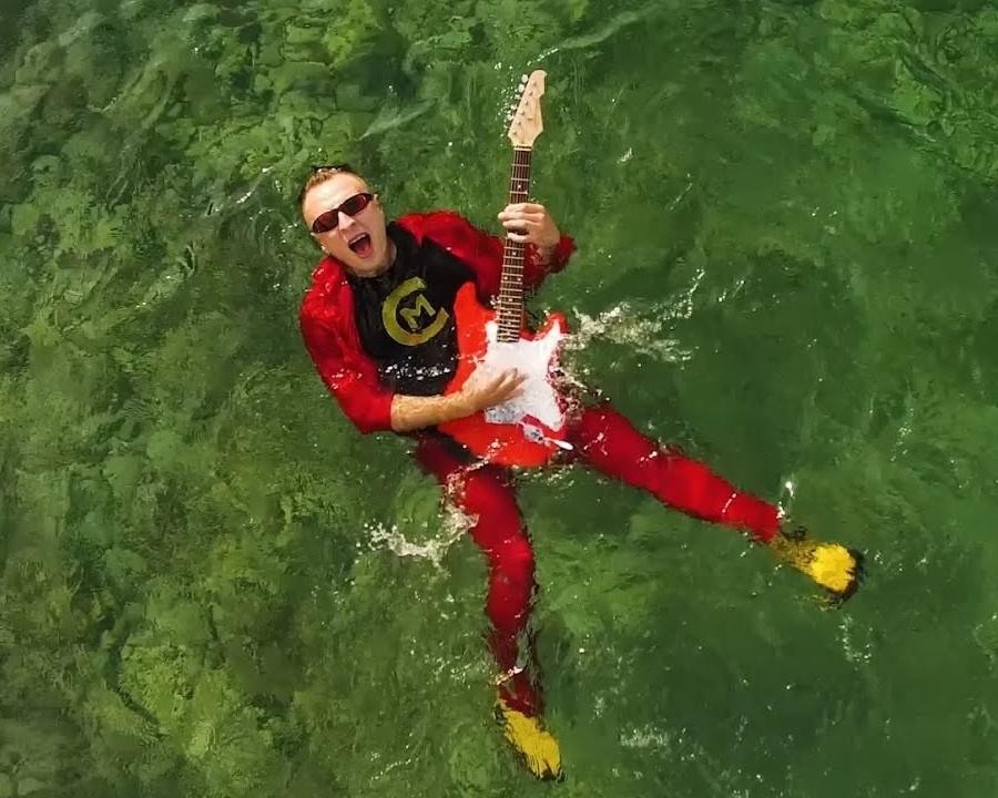 Czadoman w zbliżeniu na scenie, śpiewający do mikrofonu, z energicznym wyrazem twarzy, na tle rozmytych świateł koncertowych.