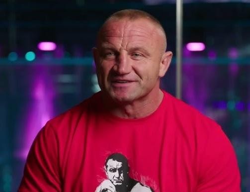 Mariusz Pudzianowski w akcji podczas walki MMA w oktagonie, prezentujący swoją muskulaturę i intensywne skupienie.