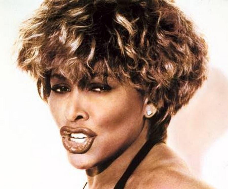 Tina Turner w zbliżeniu na scenie, śpiewająca z pasją i intensywnością, ukazująca jej potężny wokal i charyzmę sceniczną w dynamicznym oświetleniu.