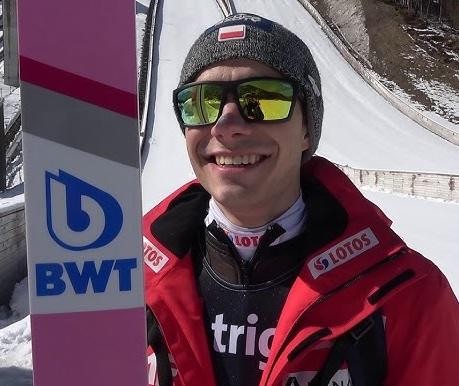 Alt: Jakub Wolny stoi na rozbiegu skoczni narciarskiej, w kombinezonie skoczka, zdeterminowany przed skokiem.